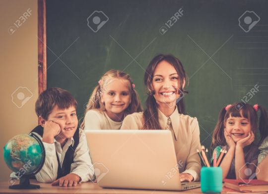 Group of happy classmates with their teacher in class near blackboard