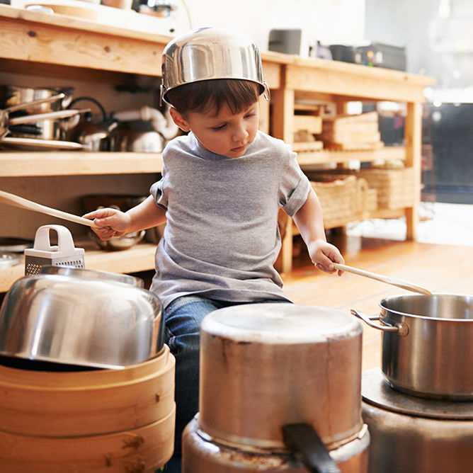 A young boy playing drums on pots and pans